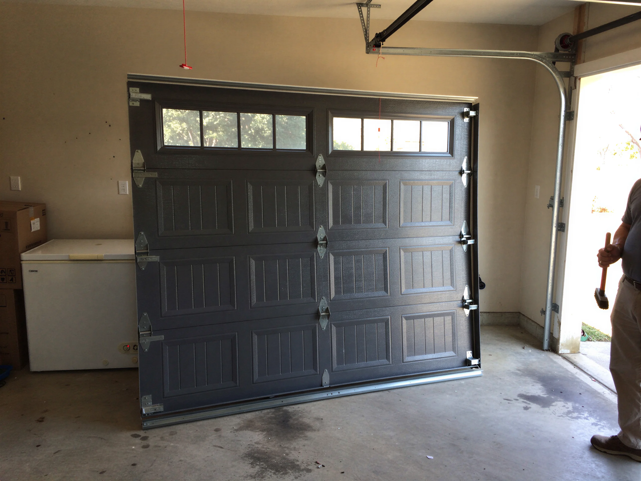 A dark gray garage door with windows is leaning against a wall inside a garage.